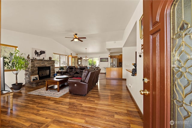 living room with hardwood / wood-style floors, ceiling fan with notable chandelier, vaulted ceiling, and a stone fireplace