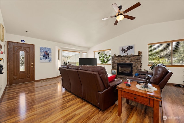 living room with hardwood / wood-style flooring, a healthy amount of sunlight, a stone fireplace, and vaulted ceiling