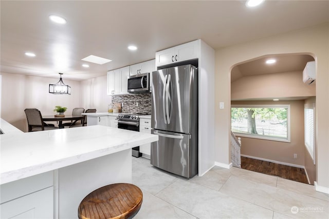 kitchen featuring appliances with stainless steel finishes, a wall unit AC, light tile patterned floors, pendant lighting, and white cabinetry