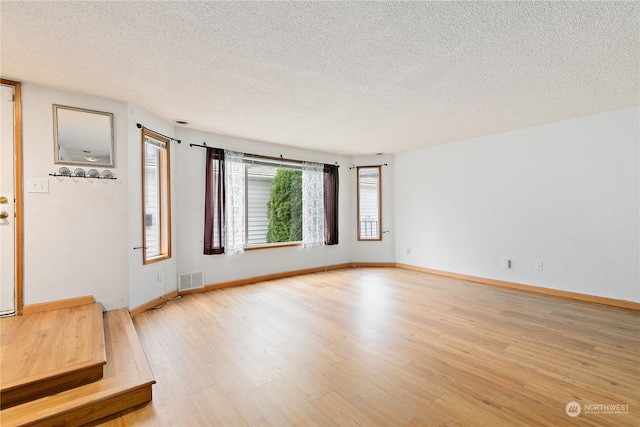 spare room with light wood-type flooring and a textured ceiling