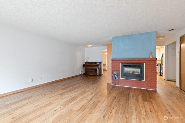 unfurnished living room with light wood-type flooring, a textured ceiling, and a brick fireplace