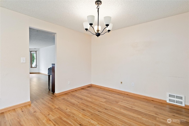 unfurnished room with hardwood / wood-style floors, a textured ceiling, and a notable chandelier