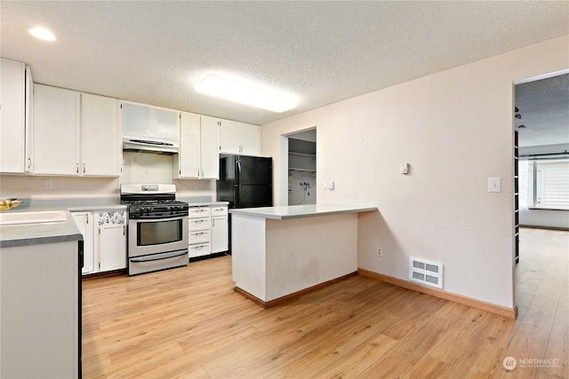 kitchen featuring stainless steel gas range oven, white cabinets, black fridge, sink, and light wood-type flooring