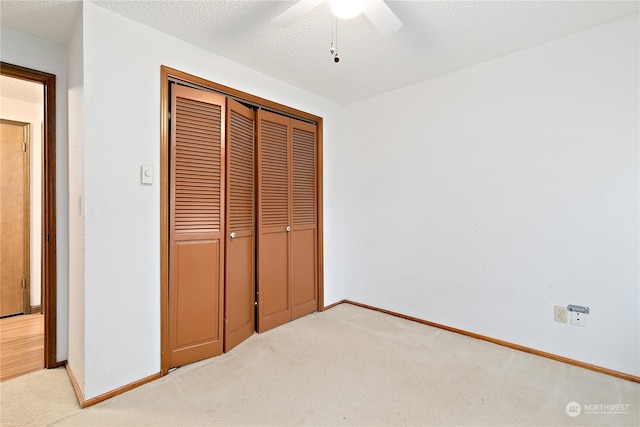 unfurnished bedroom with a textured ceiling, a closet, ceiling fan, and light colored carpet