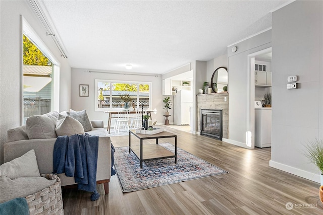 living room featuring a tile fireplace, wood-type flooring, a textured ceiling, and washer / clothes dryer