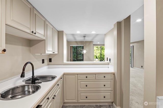 kitchen with pendant lighting, sink, light colored carpet, and cream cabinetry