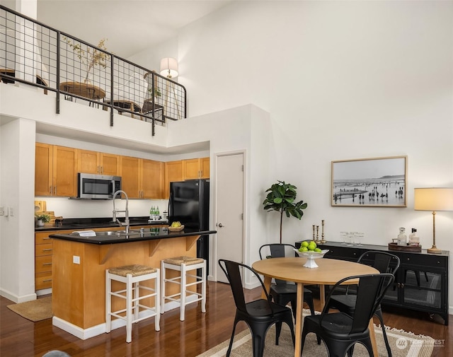 kitchen featuring dark wood-type flooring, black fridge, an island with sink, a towering ceiling, and a breakfast bar area