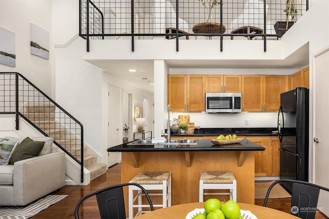 kitchen with sink, dark hardwood / wood-style flooring, a towering ceiling, a breakfast bar area, and black refrigerator