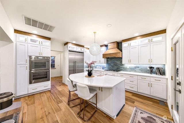 kitchen featuring a kitchen island, white cabinets, pendant lighting, and premium range hood