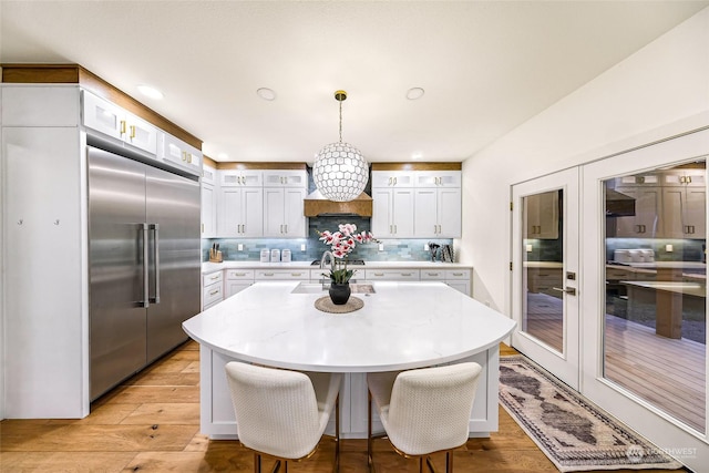 kitchen with a center island, white cabinetry, built in refrigerator, hanging light fixtures, and tasteful backsplash