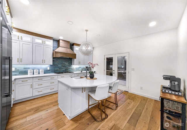 kitchen with a center island with sink, sink, white cabinetry, pendant lighting, and custom range hood