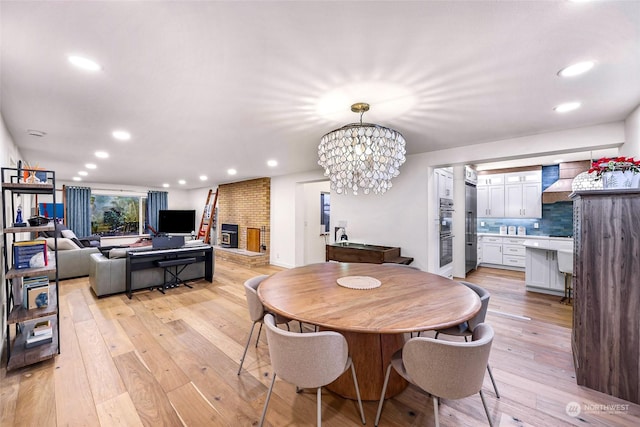 dining space featuring a brick fireplace, a notable chandelier, and light hardwood / wood-style flooring