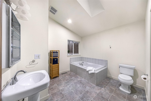 bathroom featuring sink, tiled bath, lofted ceiling, and toilet