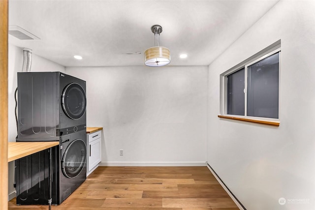 clothes washing area featuring cabinets, stacked washer / drying machine, and light hardwood / wood-style flooring