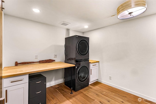 clothes washing area with cabinets, stacked washer and clothes dryer, and light hardwood / wood-style floors