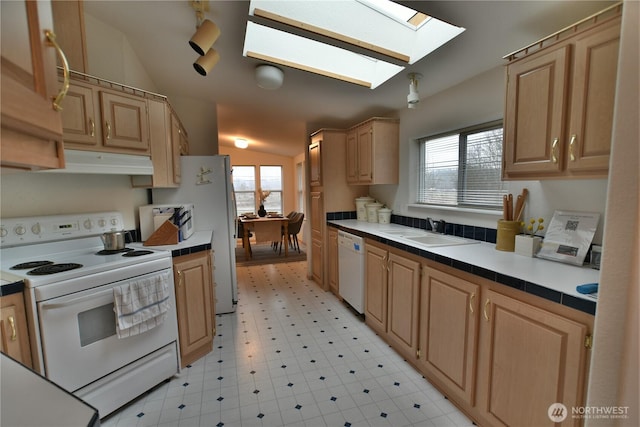 kitchen featuring light floors, lofted ceiling with skylight, a sink, white appliances, and under cabinet range hood