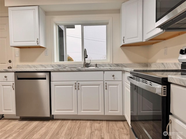 kitchen featuring sink, light stone counters, light hardwood / wood-style flooring, white cabinets, and appliances with stainless steel finishes