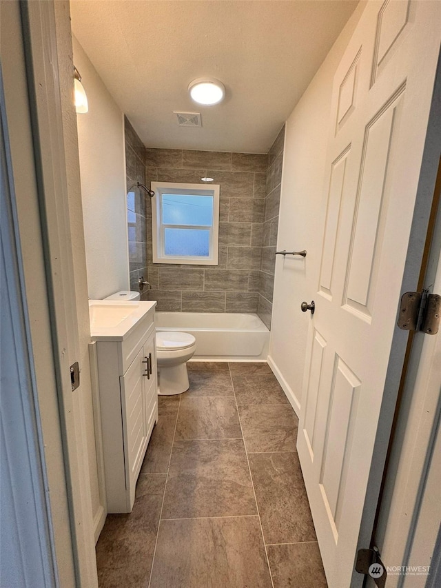 full bathroom featuring vanity, tile patterned floors, tiled shower / bath, toilet, and a textured ceiling