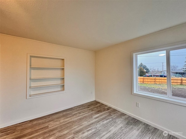 unfurnished room with hardwood / wood-style floors, a textured ceiling, and built in features