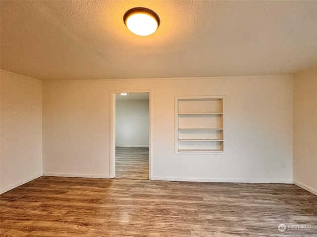 empty room featuring built in features, wood-type flooring, and a textured ceiling