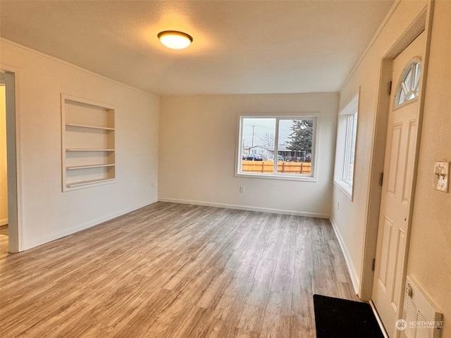 spare room featuring built in shelves, light wood-type flooring, a textured ceiling, and radiator