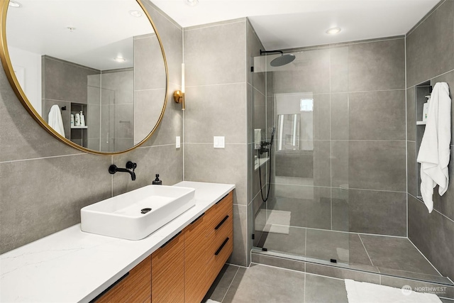 bathroom with tile patterned floors, vanity, tiled shower, and tile walls