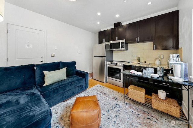 kitchen featuring backsplash, sink, light hardwood / wood-style flooring, dark brown cabinetry, and stainless steel appliances