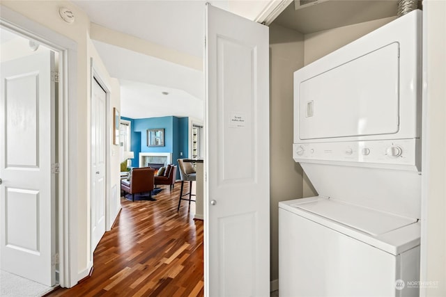 laundry area with stacked washing maching and dryer and dark wood-type flooring