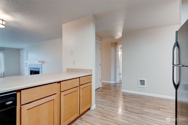 kitchen with light brown cabinetry, light wood-type flooring, black fridge, a textured ceiling, and a tile fireplace