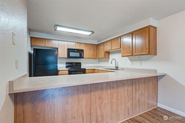 kitchen with kitchen peninsula, hardwood / wood-style floors, sink, and black appliances