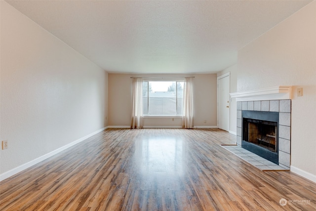 unfurnished living room with a tiled fireplace, light hardwood / wood-style flooring, and a textured ceiling