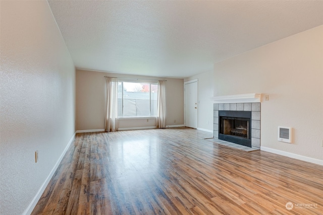 unfurnished living room featuring a tiled fireplace, a textured ceiling, and light hardwood / wood-style flooring