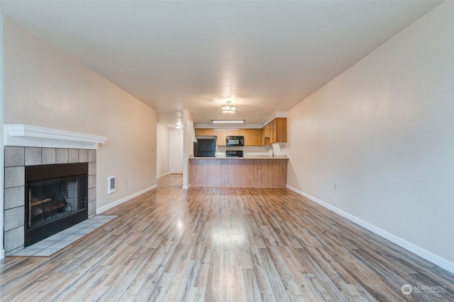 unfurnished living room featuring light hardwood / wood-style floors and a tiled fireplace