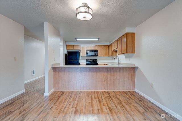 kitchen with kitchen peninsula, a textured ceiling, light hardwood / wood-style floors, and black appliances