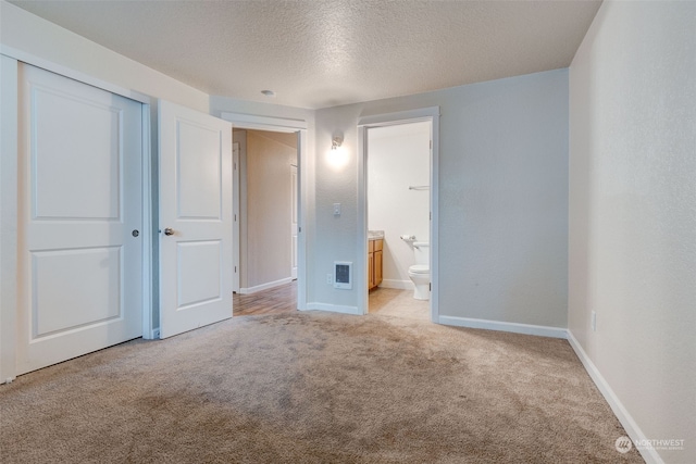 unfurnished bedroom featuring a textured ceiling, light colored carpet, ensuite bath, and a closet