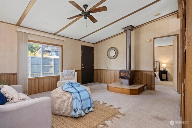 living room with light carpet, ornamental molding, ceiling fan, wooden walls, and a wood stove