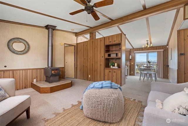 carpeted living room featuring vaulted ceiling with beams, ceiling fan with notable chandelier, a wood stove, and wooden walls