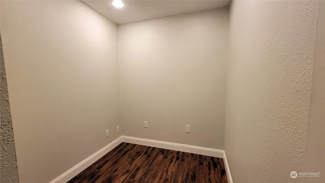 empty room featuring dark wood-style floors, baseboards, and a textured wall