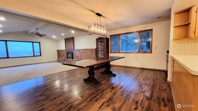 dining room featuring lofted ceiling with beams, dark wood-style floors, a fireplace, baseboards, and ceiling fan