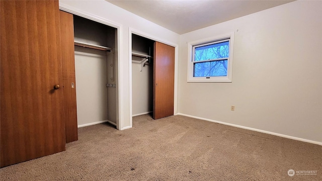 unfurnished bedroom with carpet flooring, two closets, and baseboards