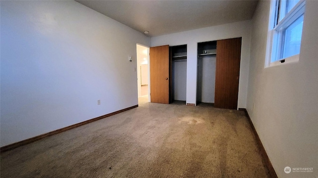 unfurnished bedroom featuring baseboards, two closets, and light carpet