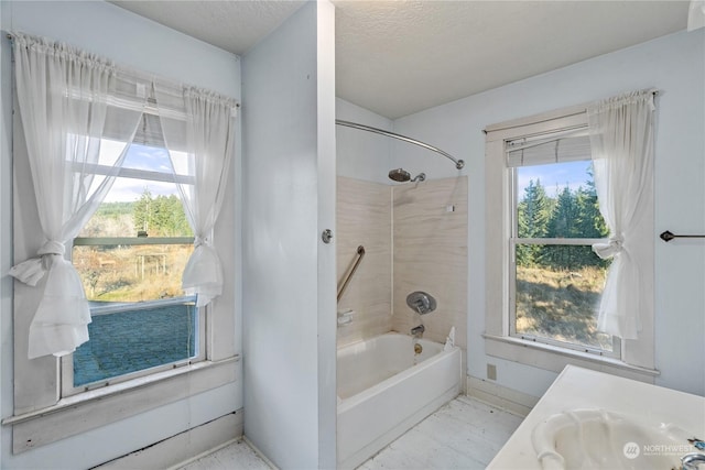 bathroom with a textured ceiling, vanity, a healthy amount of sunlight, and tiled shower / bath combo