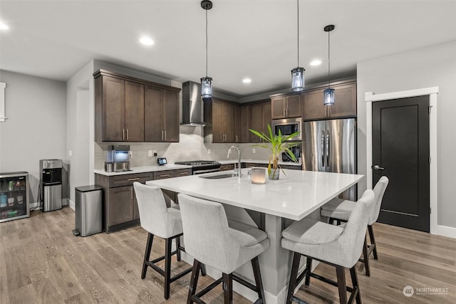 kitchen featuring dark brown cabinetry, sink, wall chimney exhaust hood, and pendant lighting