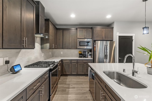 kitchen featuring appliances with stainless steel finishes, tasteful backsplash, wall chimney exhaust hood, sink, and hanging light fixtures