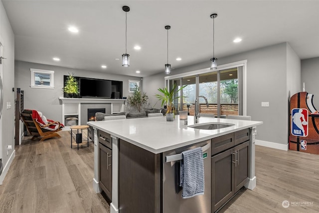 kitchen with dishwasher, sink, hanging light fixtures, light wood-type flooring, and an island with sink