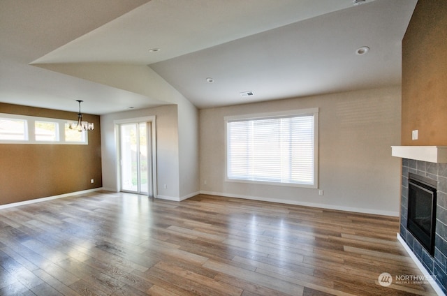 unfurnished living room featuring lofted ceiling, a fireplace, light hardwood / wood-style floors, and an inviting chandelier