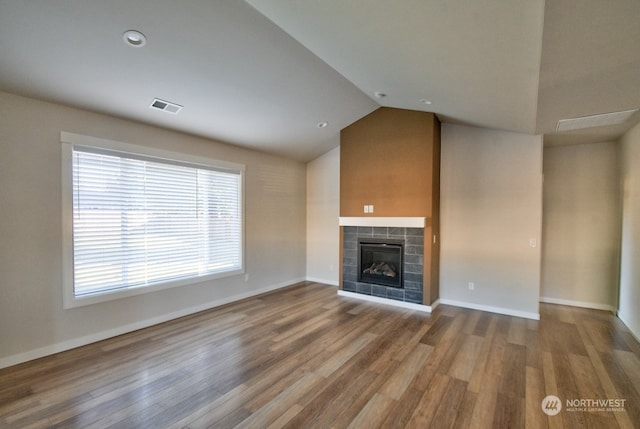 unfurnished living room featuring a tiled fireplace, lofted ceiling, and hardwood / wood-style floors