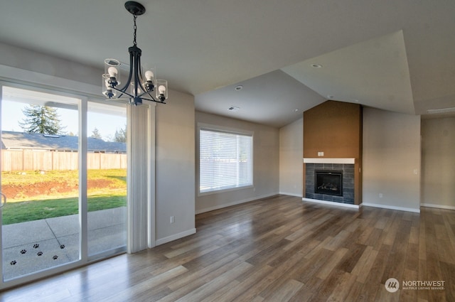 unfurnished living room featuring an inviting chandelier, lofted ceiling, wood-type flooring, and a tiled fireplace