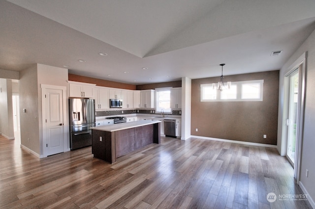 kitchen featuring sink, appliances with stainless steel finishes, white cabinetry, a center island, and decorative light fixtures