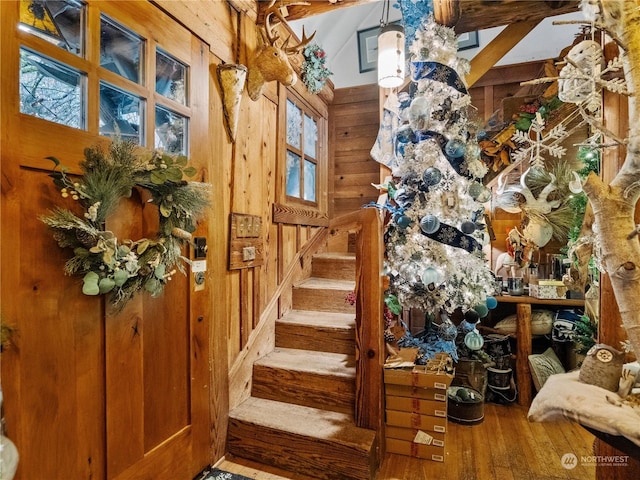 stairway with wood-type flooring, beam ceiling, a wealth of natural light, and wood walls